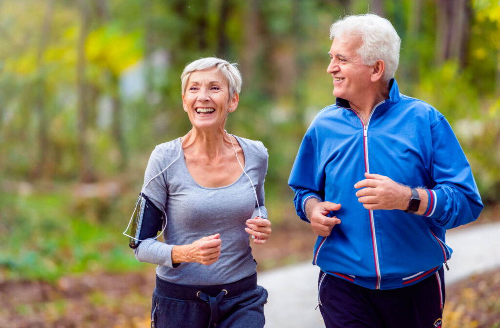 An older adult man and an older adult woman smiling while jogging outdoors.