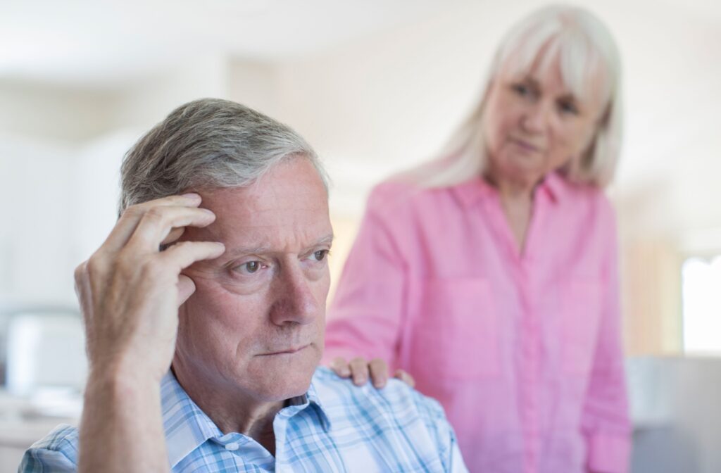 A senior places their hand on their spouse’s shoulder, concerned about their withdrawal after a dementia diagnosis