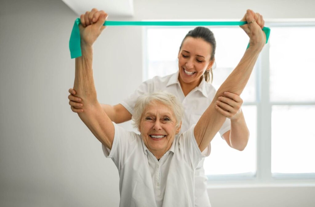 A physiotherapist helps an older adult perform strengthening exercises for their arm using an elastic band.